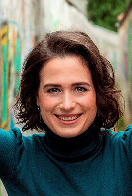 Das Portrait zeigt Robin Ziehbrunner mit schulterlangen, welligen, braunen Haaren und einem freundlichen Lächeln.